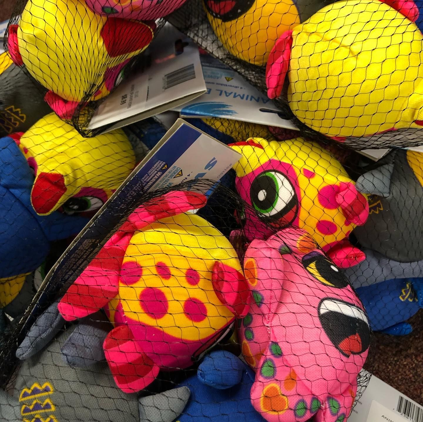 Pile of colorful fish-shaped dog toys in net bags; yellow, pink, and blue with spots and googly eyes.