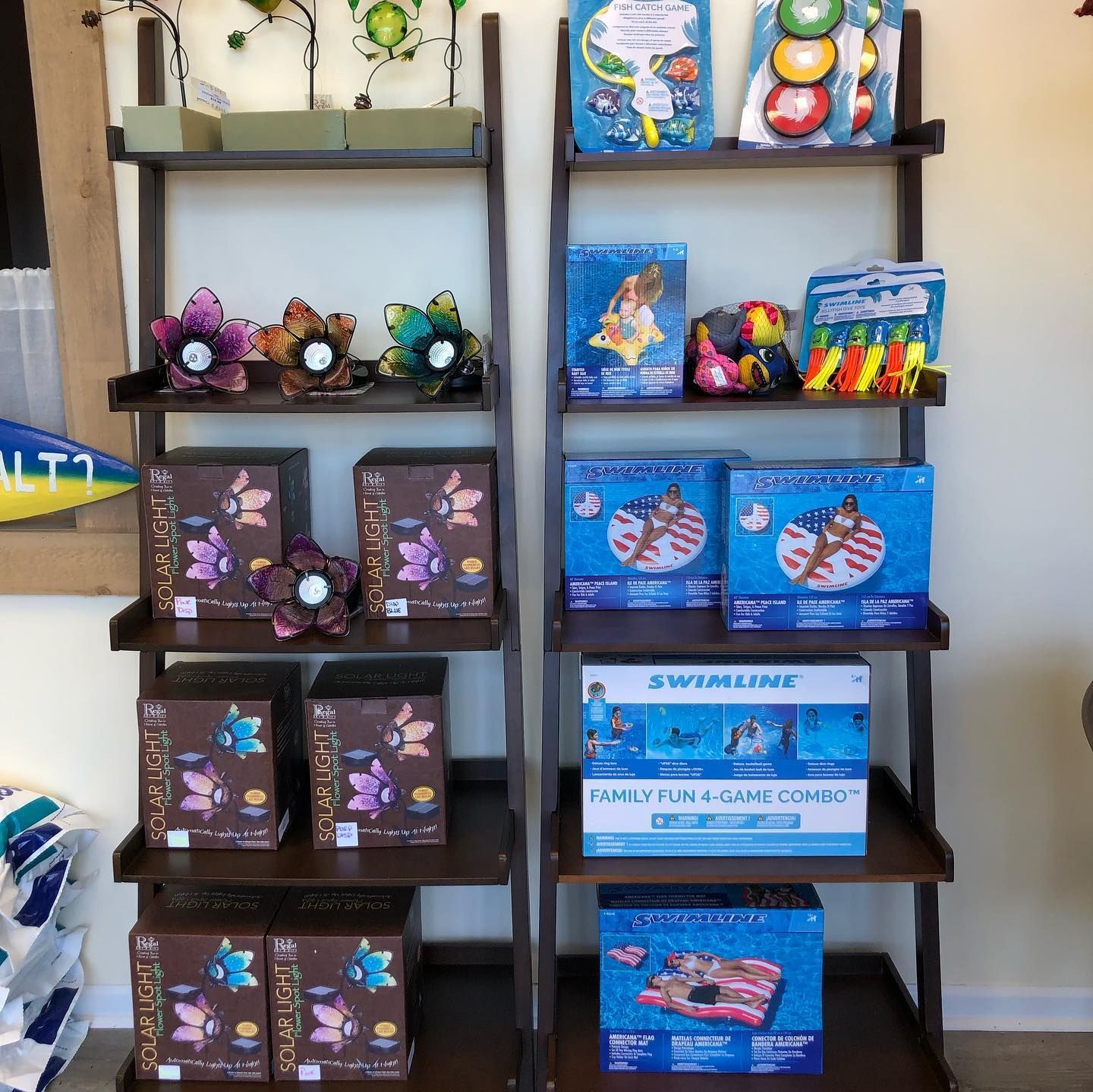 Two wooden ladder shelves displaying various pool floats and decorative flowers.