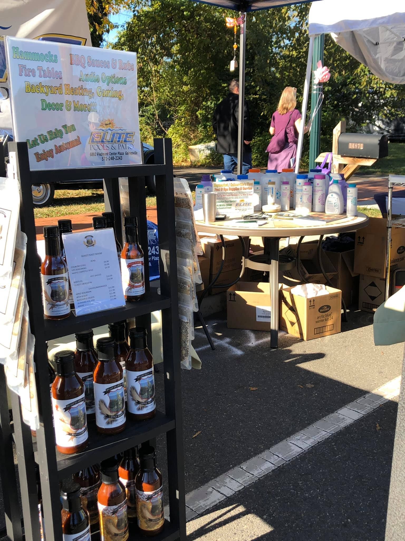 Bottles of barbecue sauce on display at a market stall. People browse in the background.