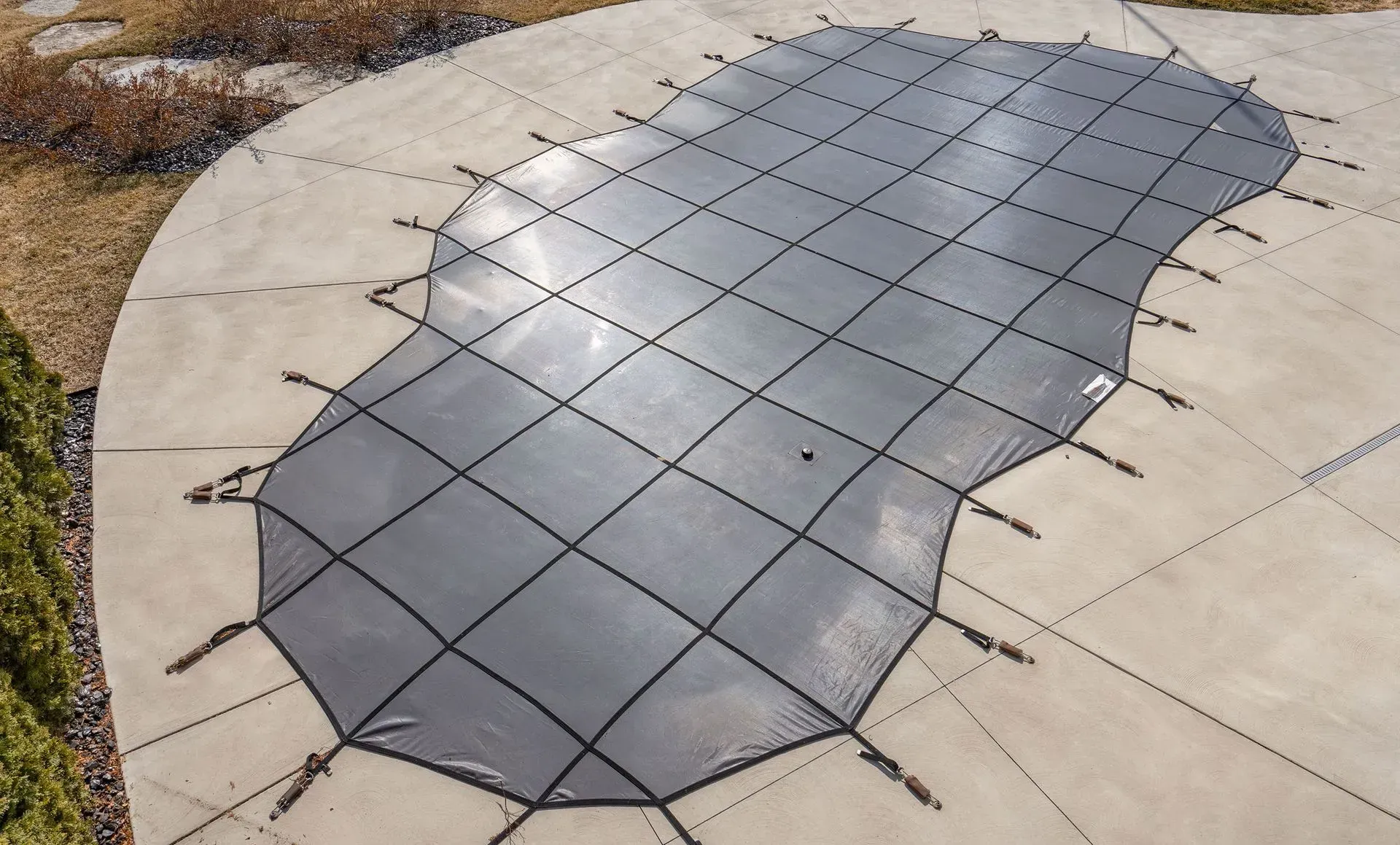 Black mesh pool cover stretched over a kidney-shaped pool.