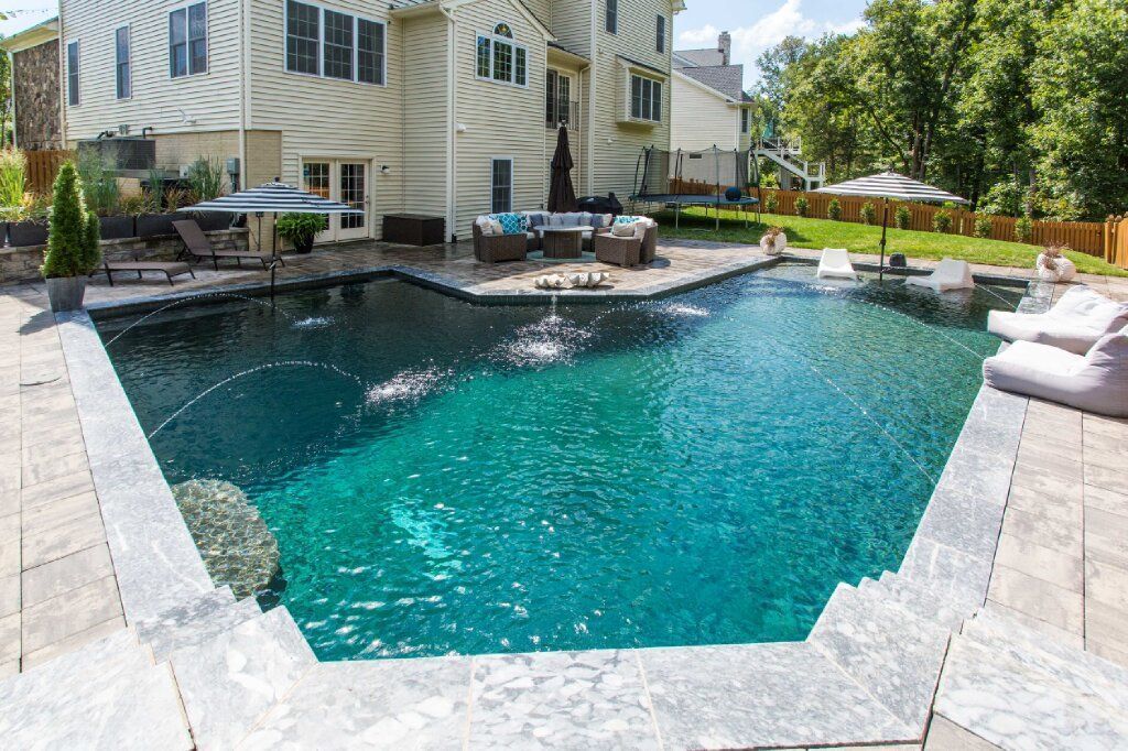 Blue pool cover on an outdoor swimming pool, tan concrete deck, trees and blue sky background.