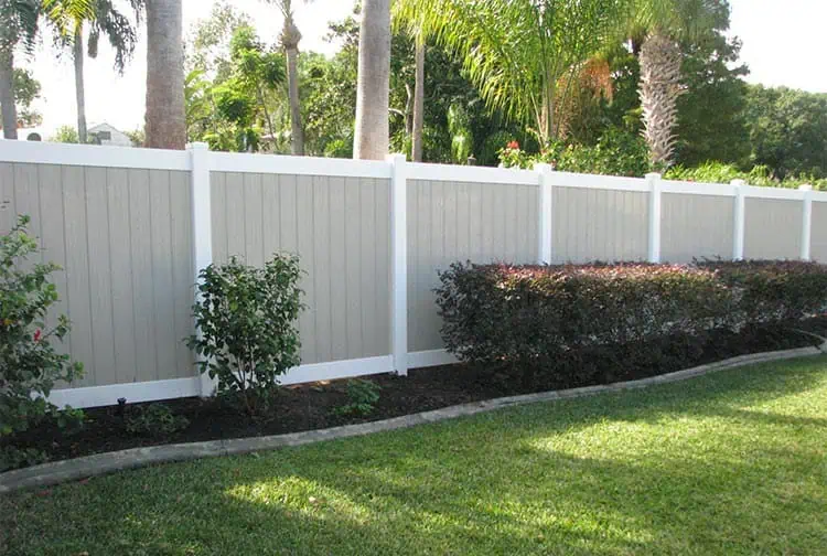 A white and tan fence surrounds a lush green yard.