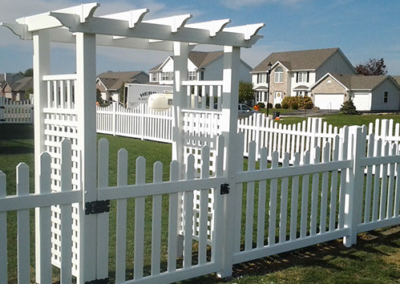 A white picket fence with a pergola in the background
