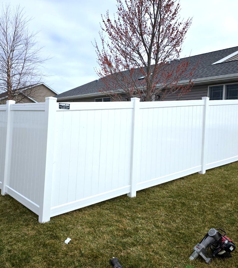 A white vinyl fence is sitting in the grass in front of a house.