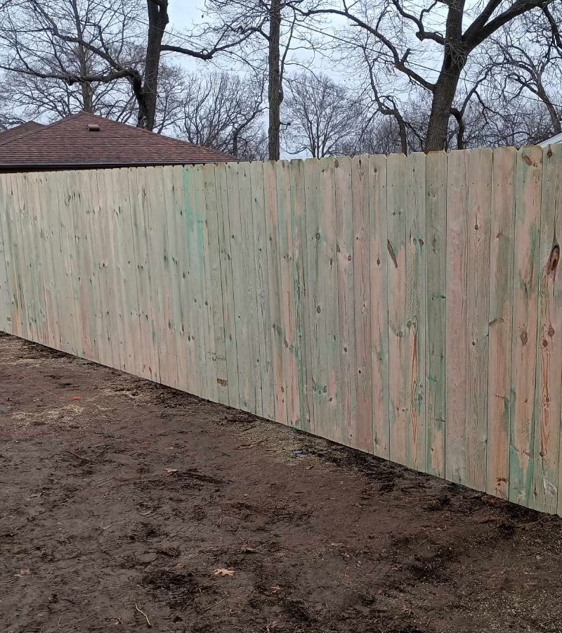 A wooden fence is sitting in the dirt in front of a house.