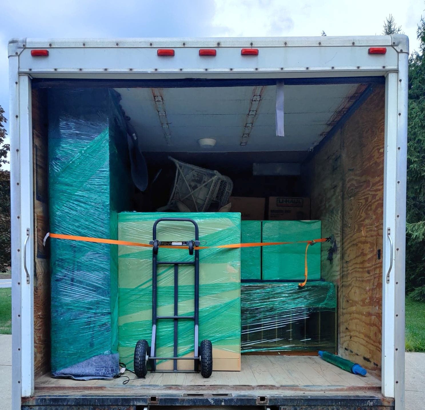 Moving truck cargo area packed with furniture and boxes, secured with straps.