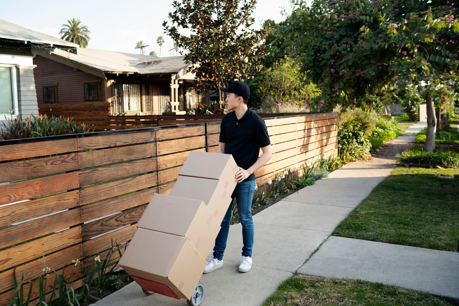 A man is pushing a cart with boxes on it down a sidewalk.