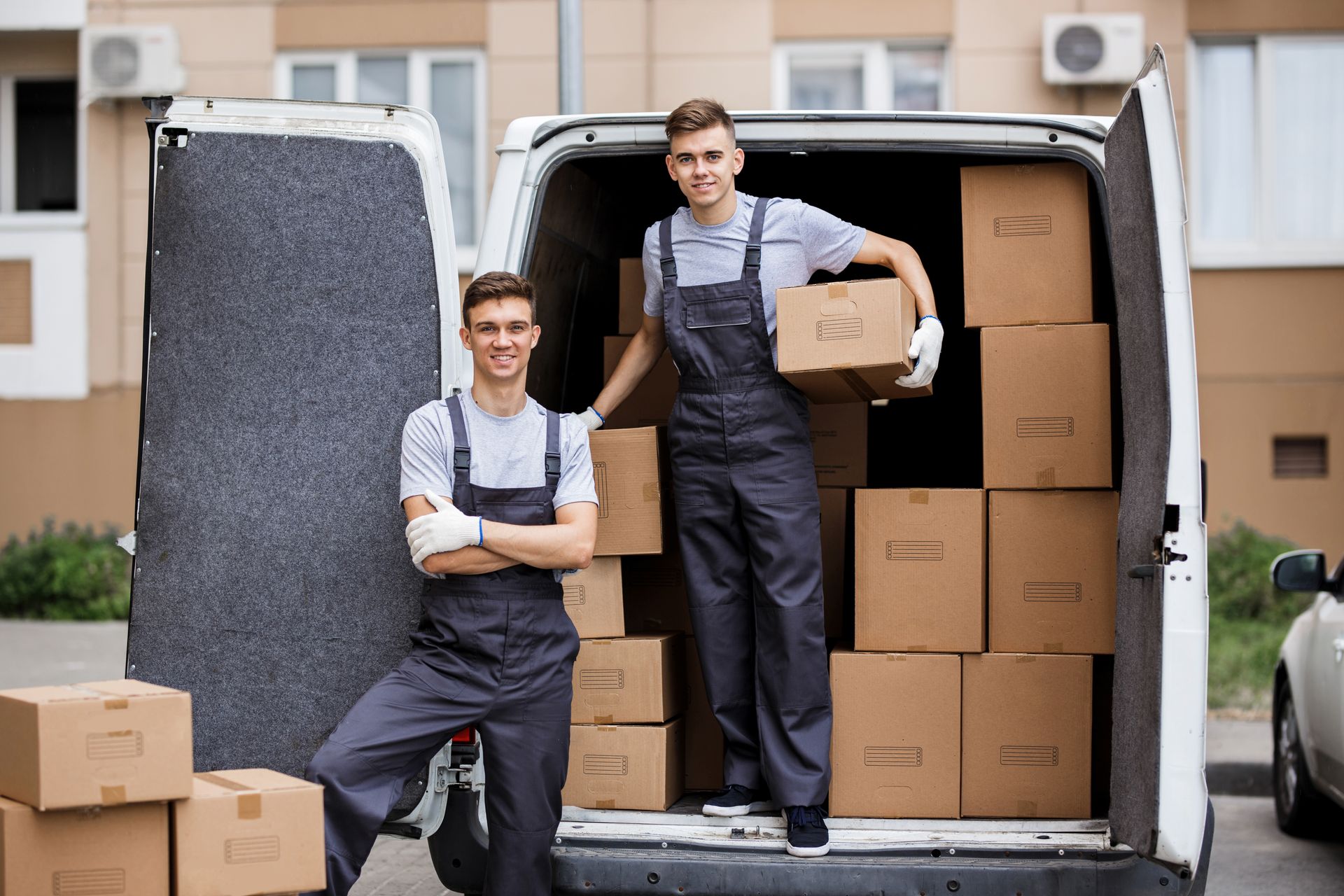 Two men are standing in front of a van filled with boxes.
