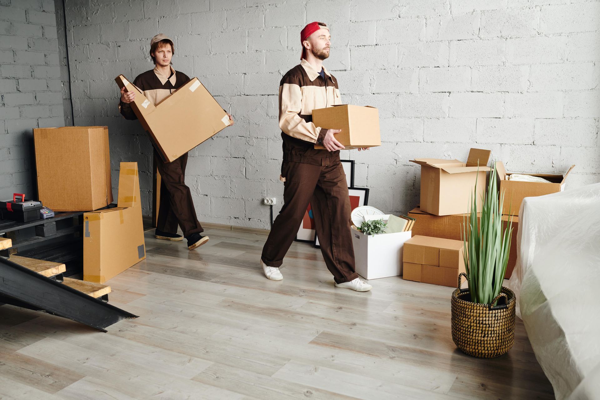 Two men are carrying cardboard boxes in a living room.