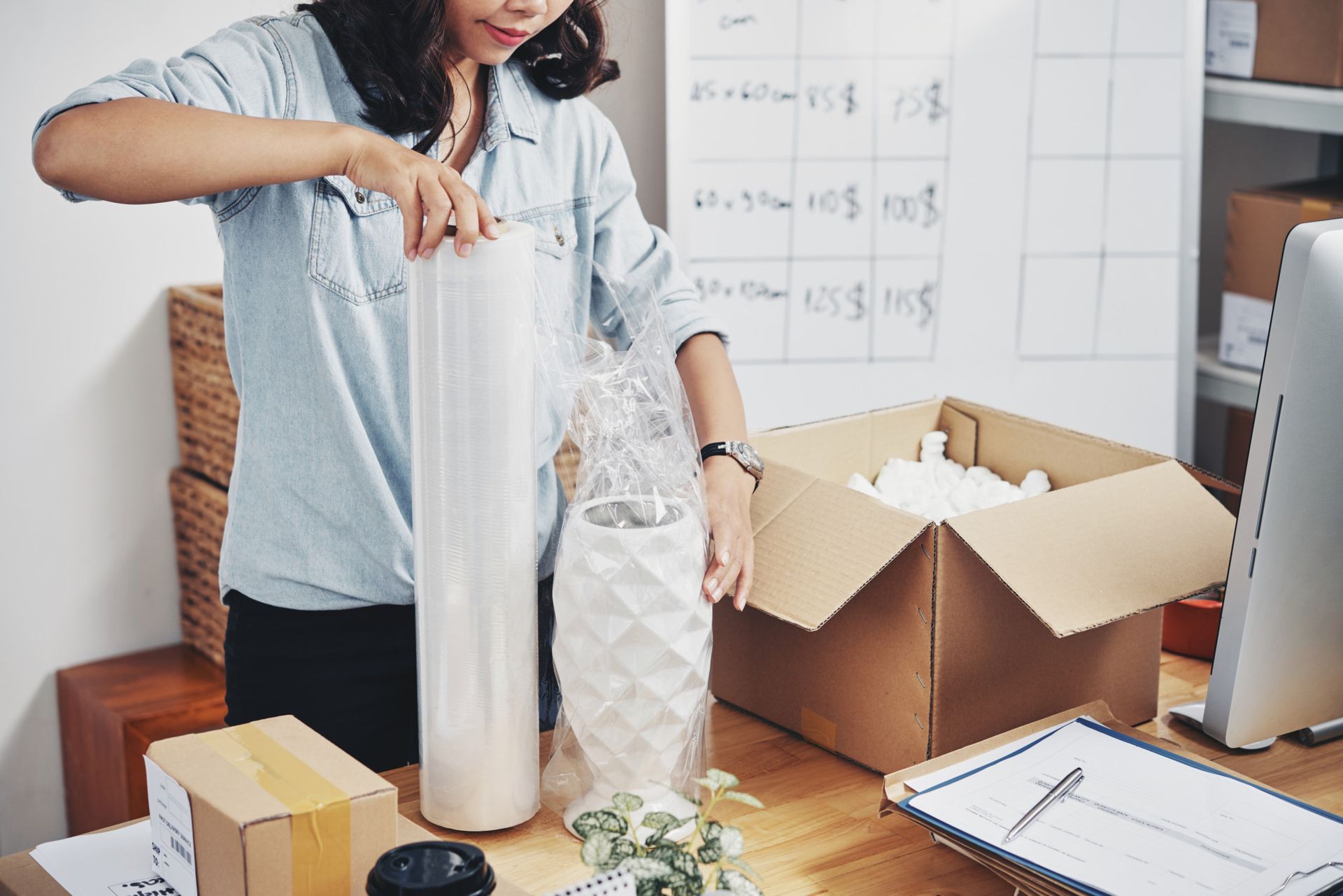 A woman is wrapping a vase in plastic wrap.