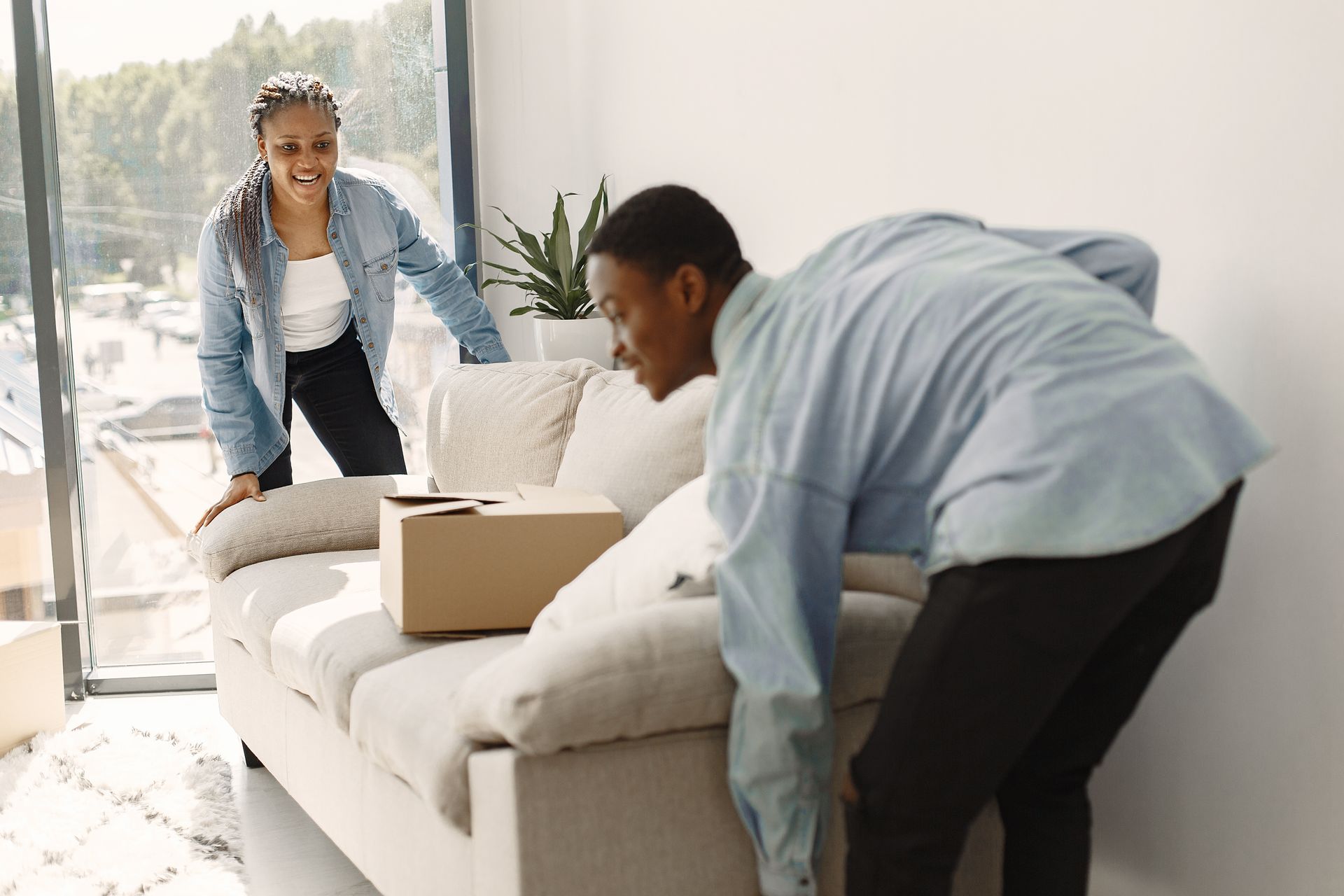 A man and a woman are moving a couch in a living room.