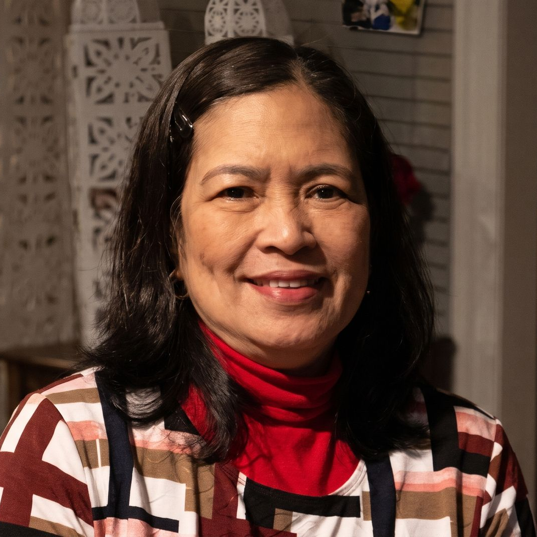 Smiling woman in a red turtleneck and plaid top, posed indoors with a decorative background.