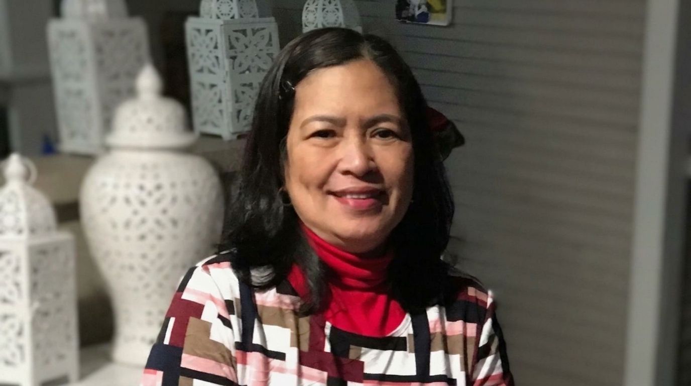 Smiling woman with dark hair wearing a red scarf and patterned top against a dark background