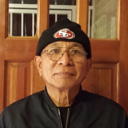 Man wearing glasses and a black beanie, standing indoors in front of wooden doors.