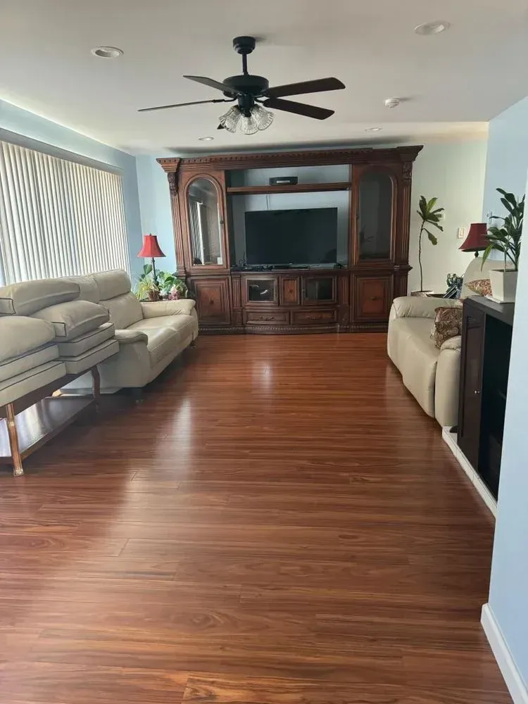 Living room with wood floors, two beige sofas, and a large dark wood entertainment center under a ceiling fan