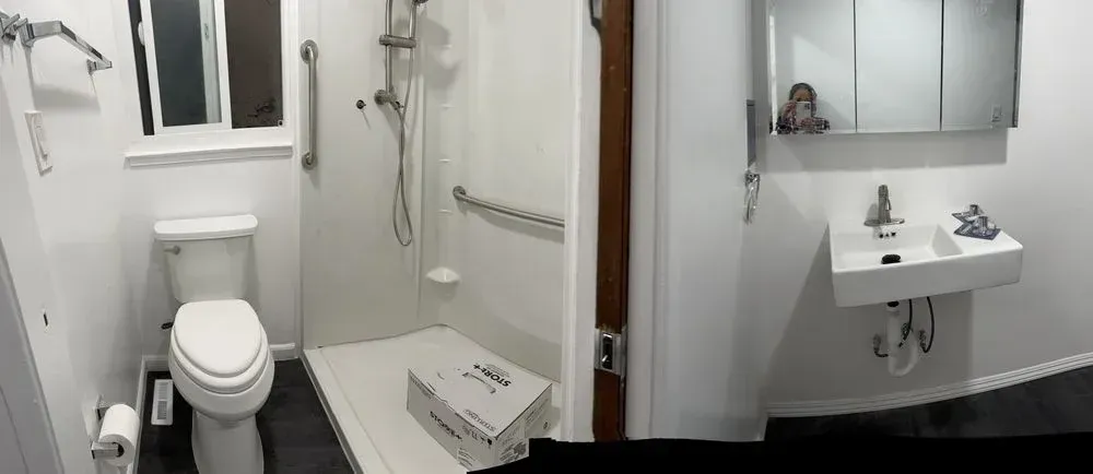 Small bathroom with toilet, shower, and wall-mounted sink in a white interior.
