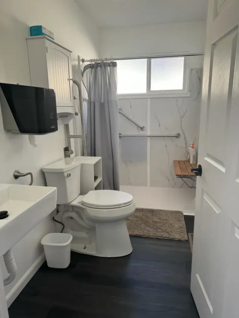 Small bathroom with a toilet, sink, shower, and dark floor, viewed from the doorway.