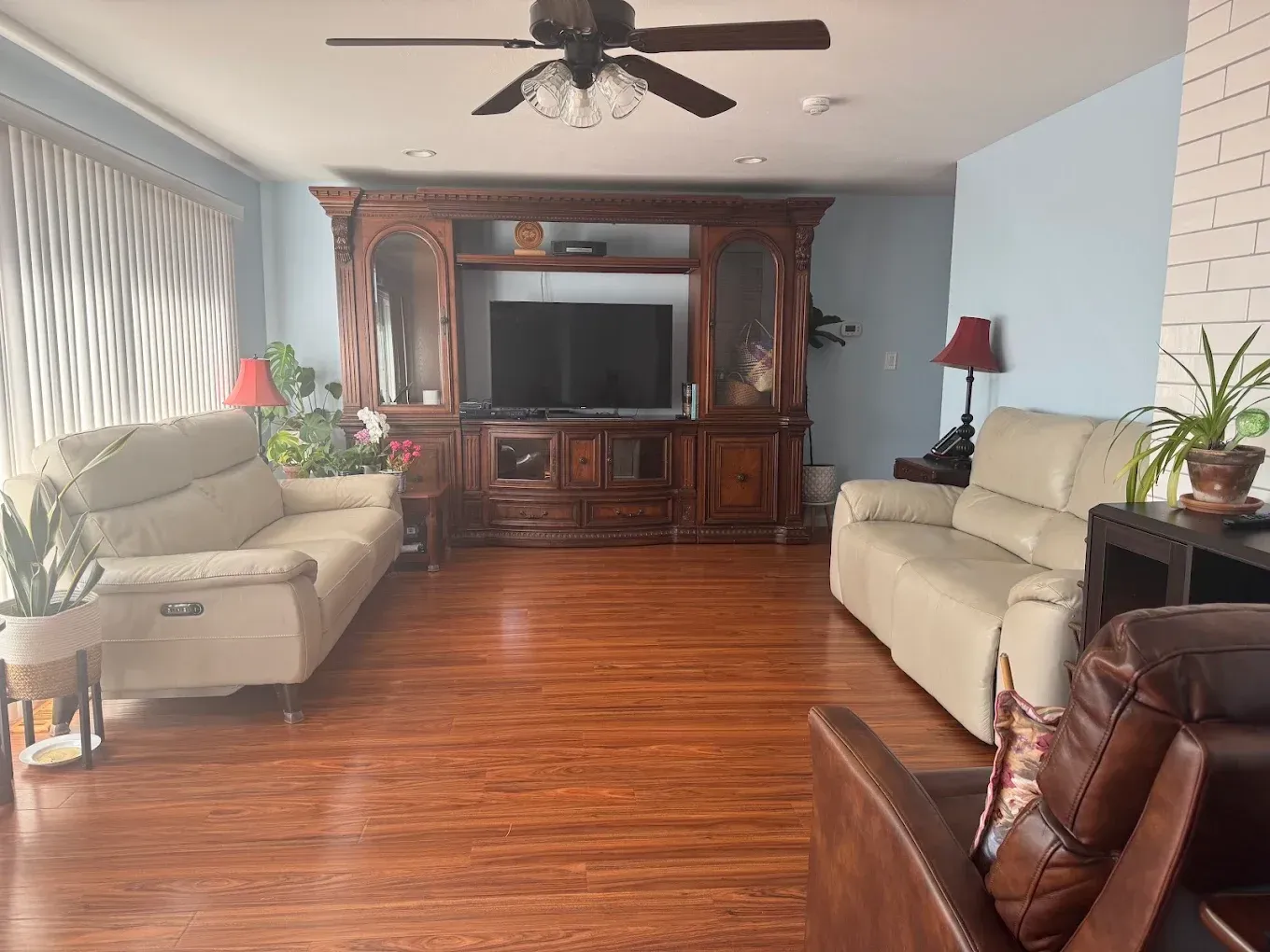 Bright living room with hardwood floors, beige sofas, and a large wooden entertainment center.