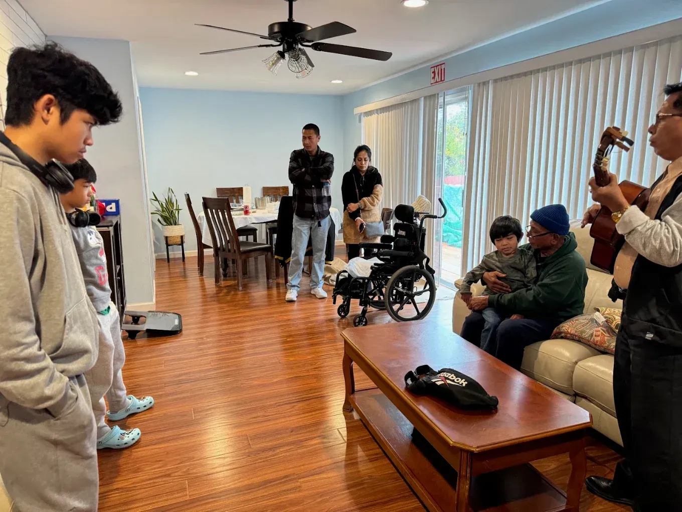 People gathered in a bright living room, with a wheelchair user near the center and others seated on a couch.