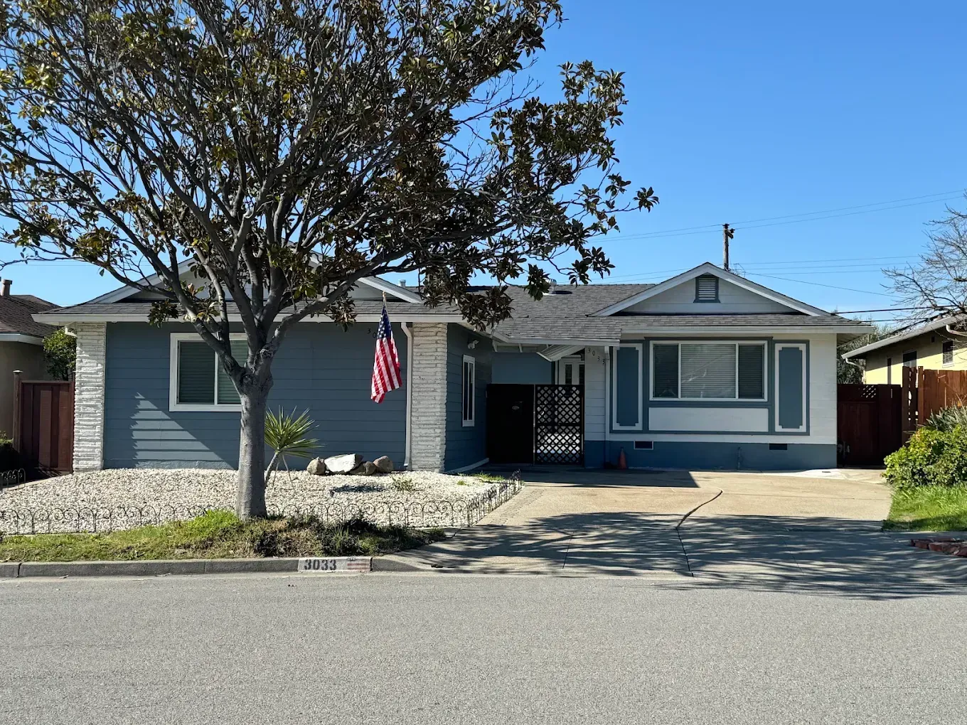 Blue single-story house with a front yard, driveway, and an American flag by the entrance