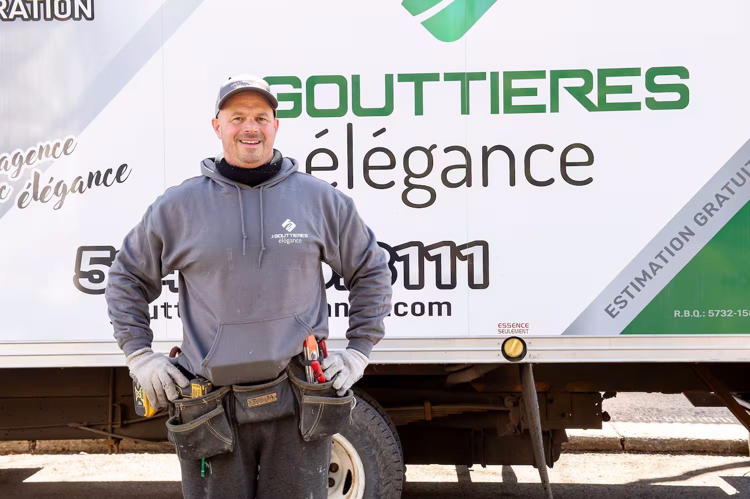 Un homme avec une ceinture à outils sourit devant un camion avec