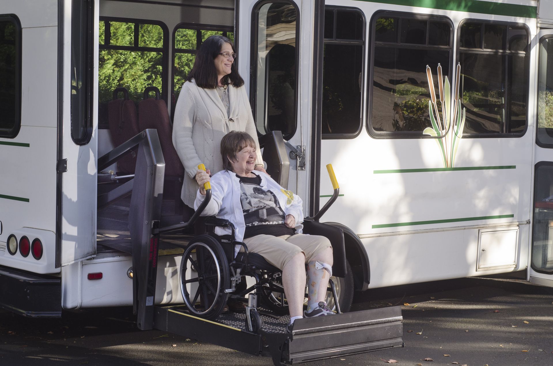 Woman assisting seated passenger in wheelchair at a bus ramp