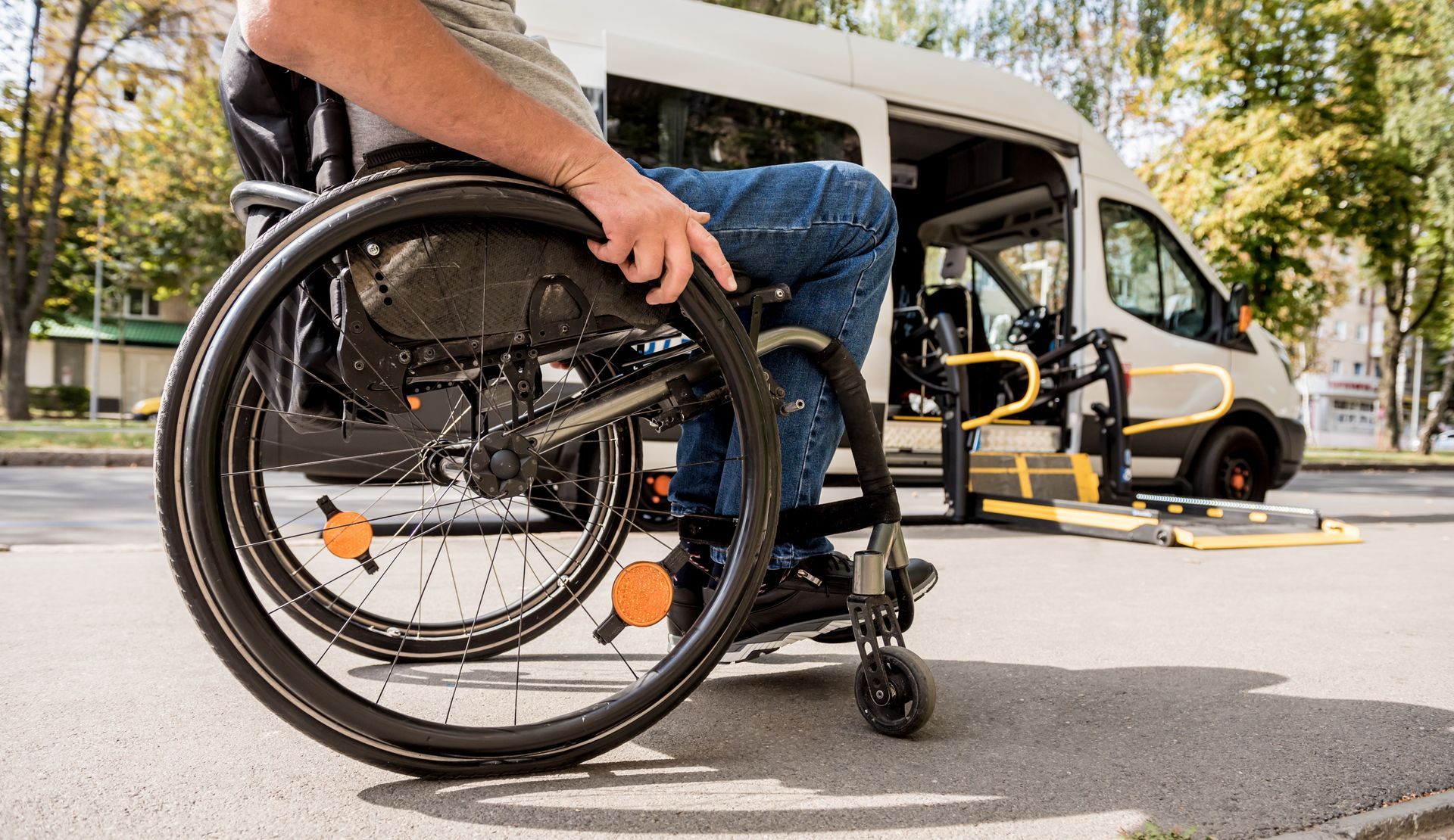 Person in a wheelchair boarding a white shuttle van at a curbside pickup point