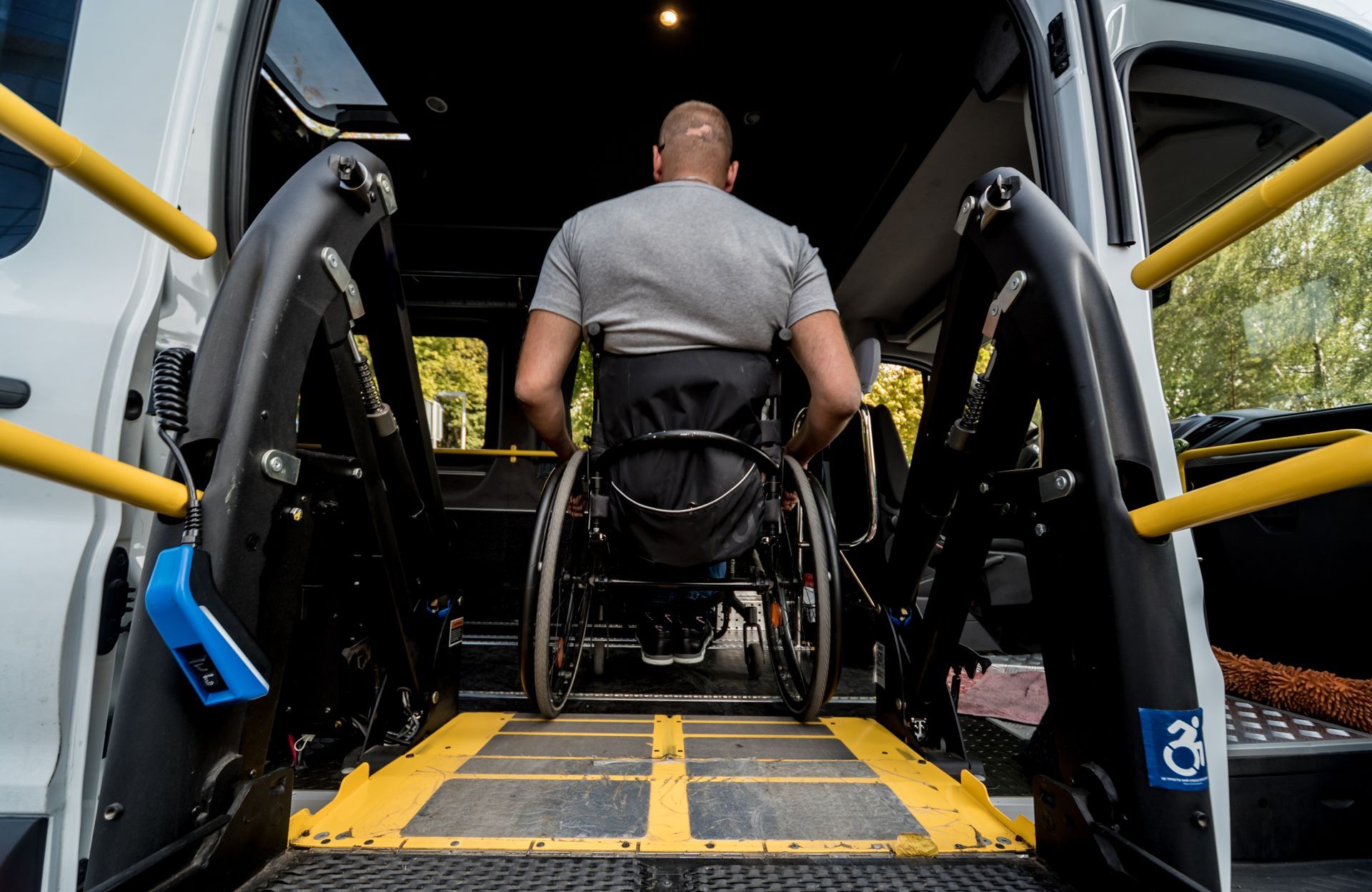 Man in a wheelchair boarding a van via an accessible ramp, with yellow handrails.