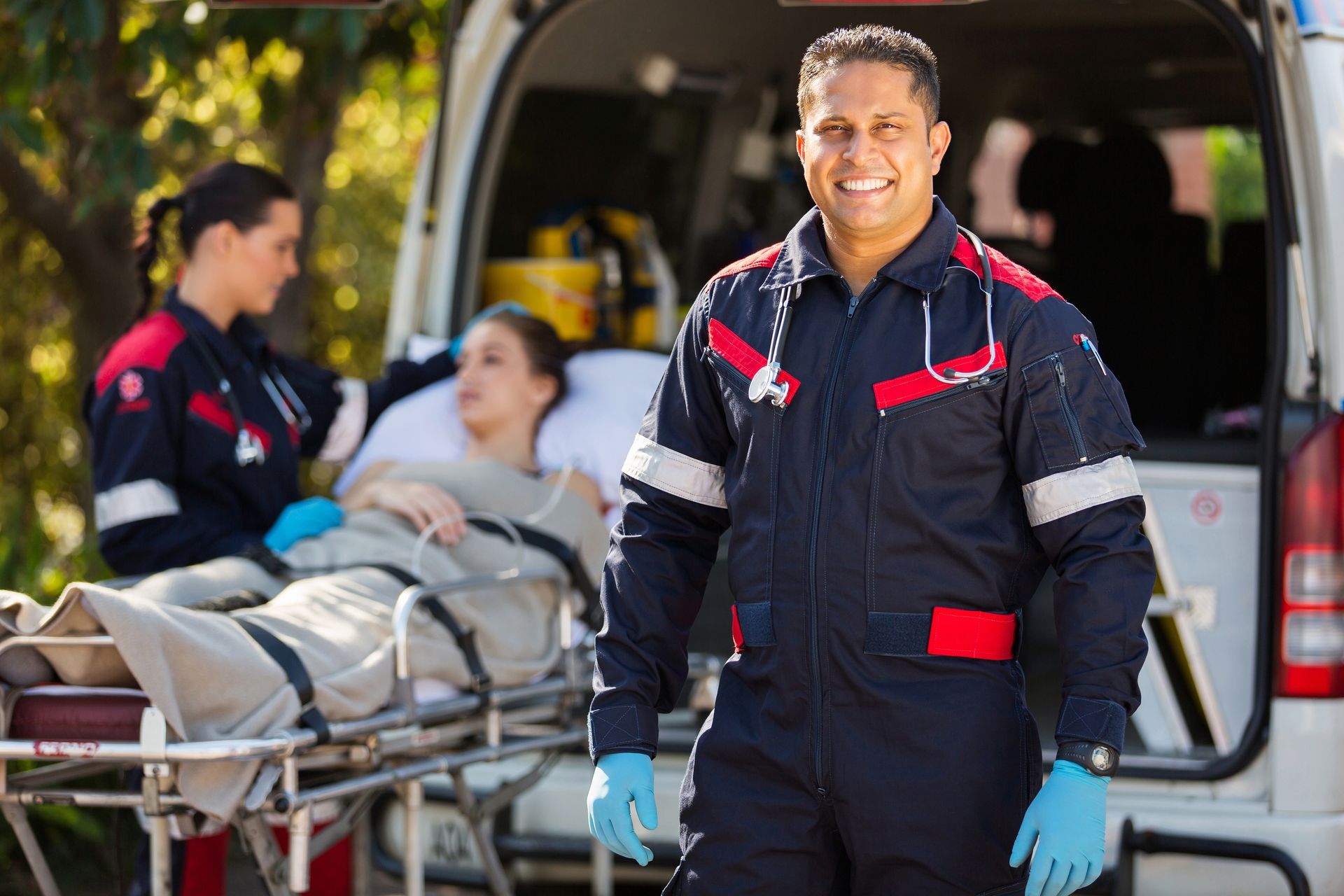 Paramedics in dark uniforms loading a patient on a stretcher into an ambulance