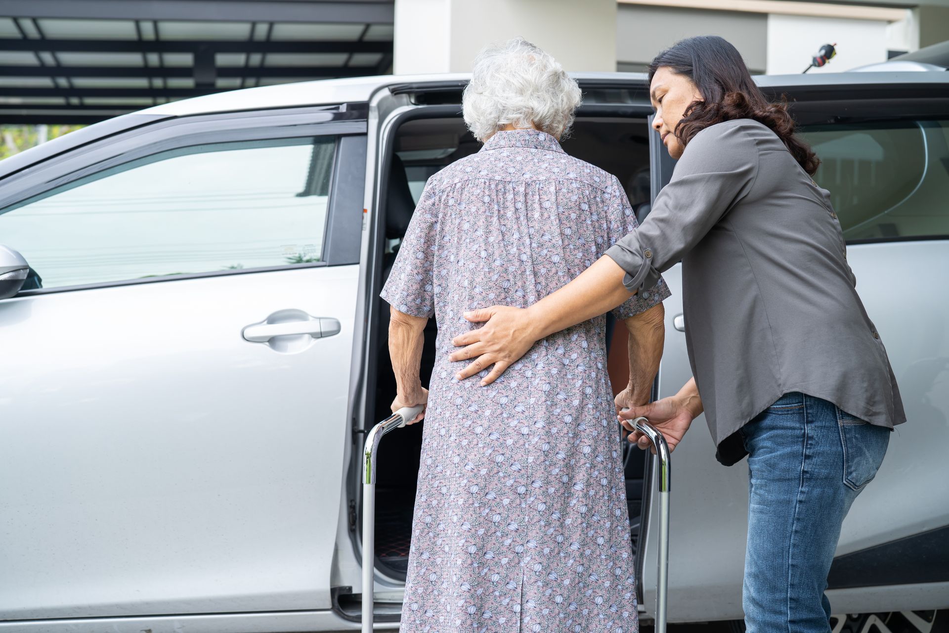 Woman helping an elderly person into a silver SUV by an open rear door
