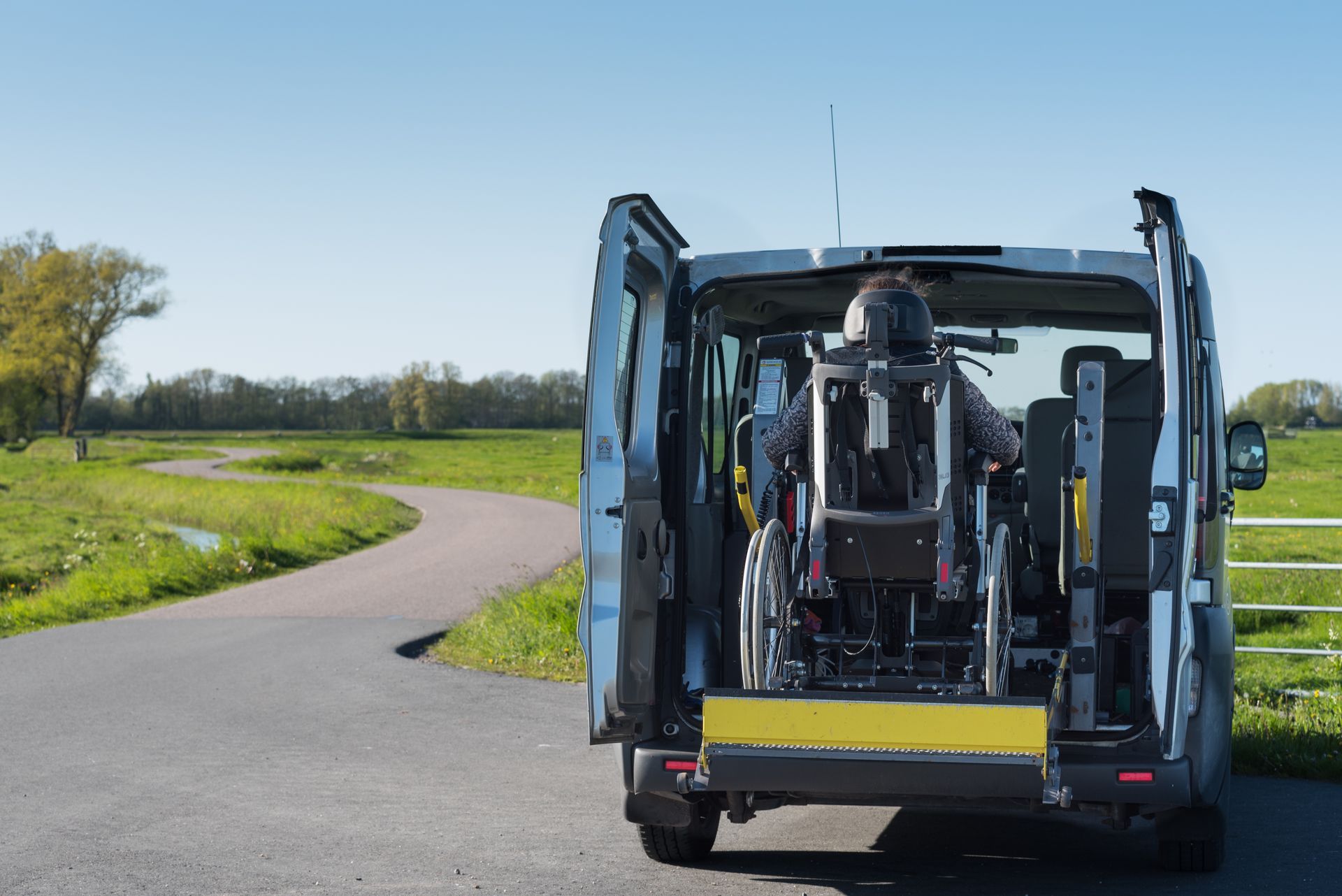 Small utility vehicle with open rear doors parked on a winding rural road beside green fields.