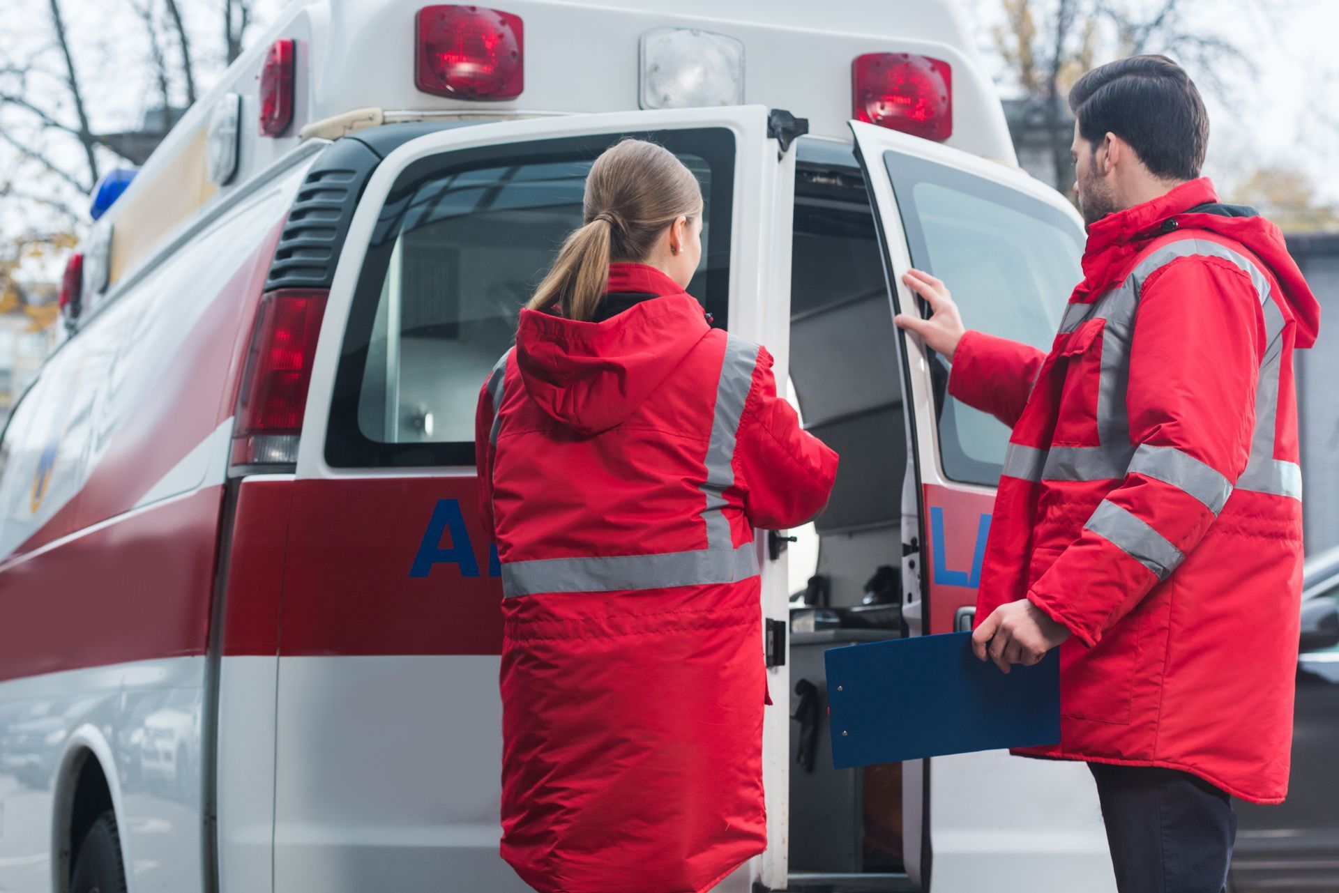 Two paramedics in red jackets loading a stretcher into an ambulance