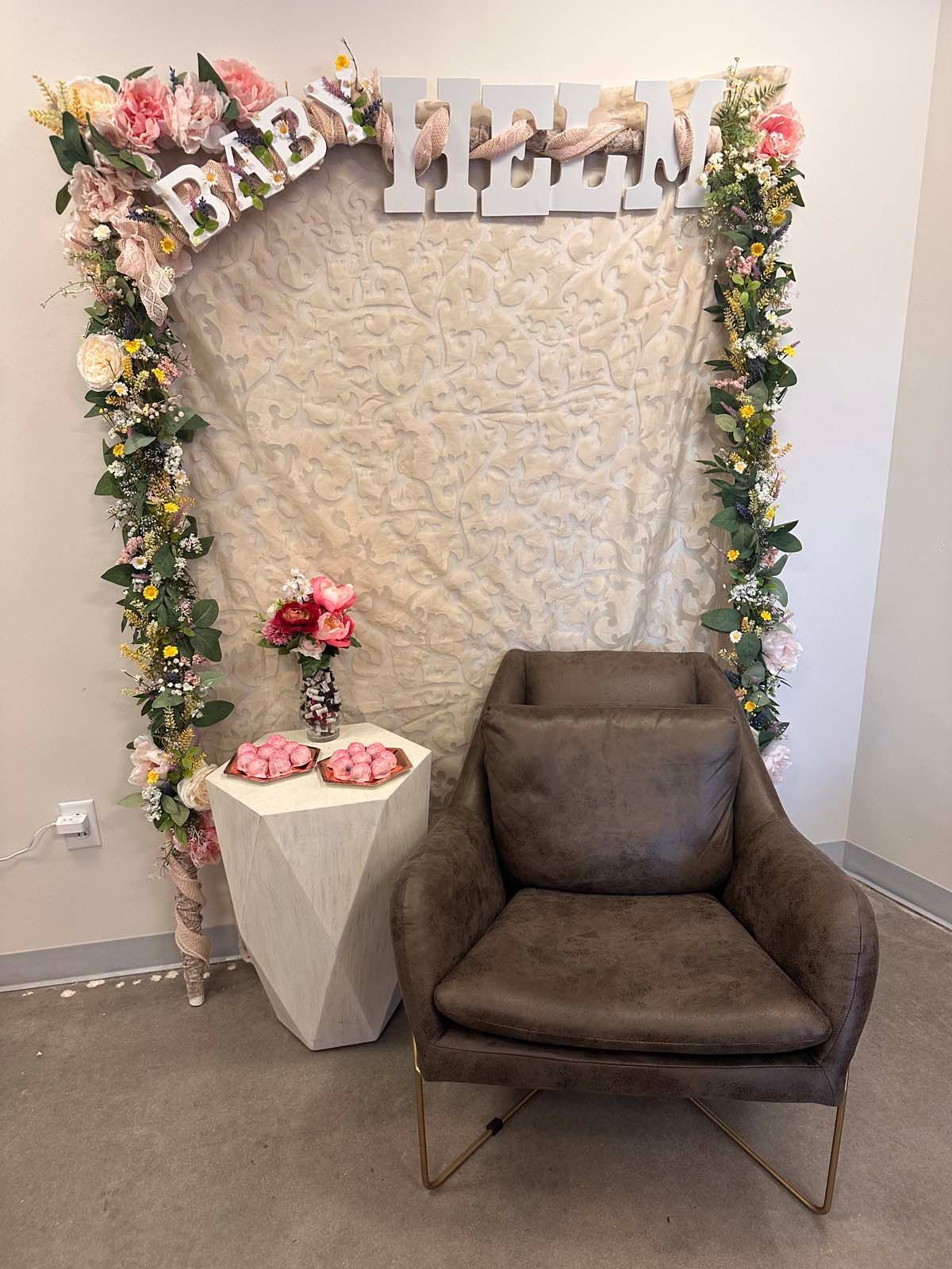 A chair is sitting in front of a baby shower backdrop.