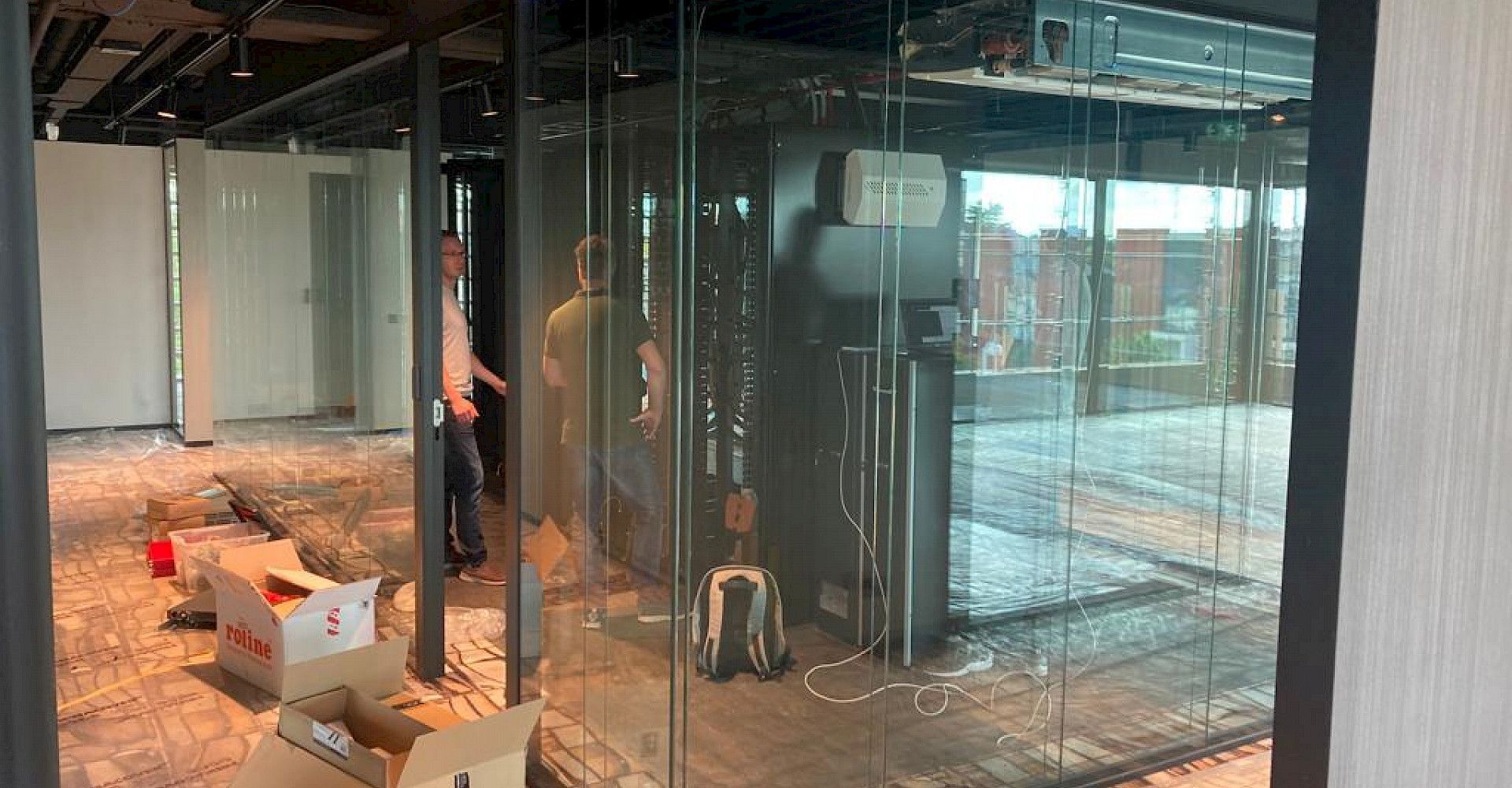 Interieur in aanbouw met glazen wanden, gereedschap en een werker bij een deuropening.