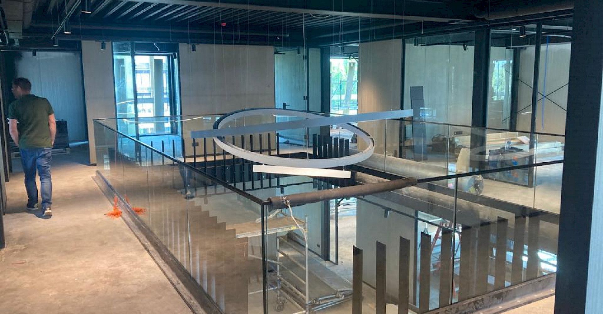 Een overdekte bouwplaats met een metalen tussenverdieping en glazen balustrade, gezien vanaf een onafgewerkte bovenverdieping.