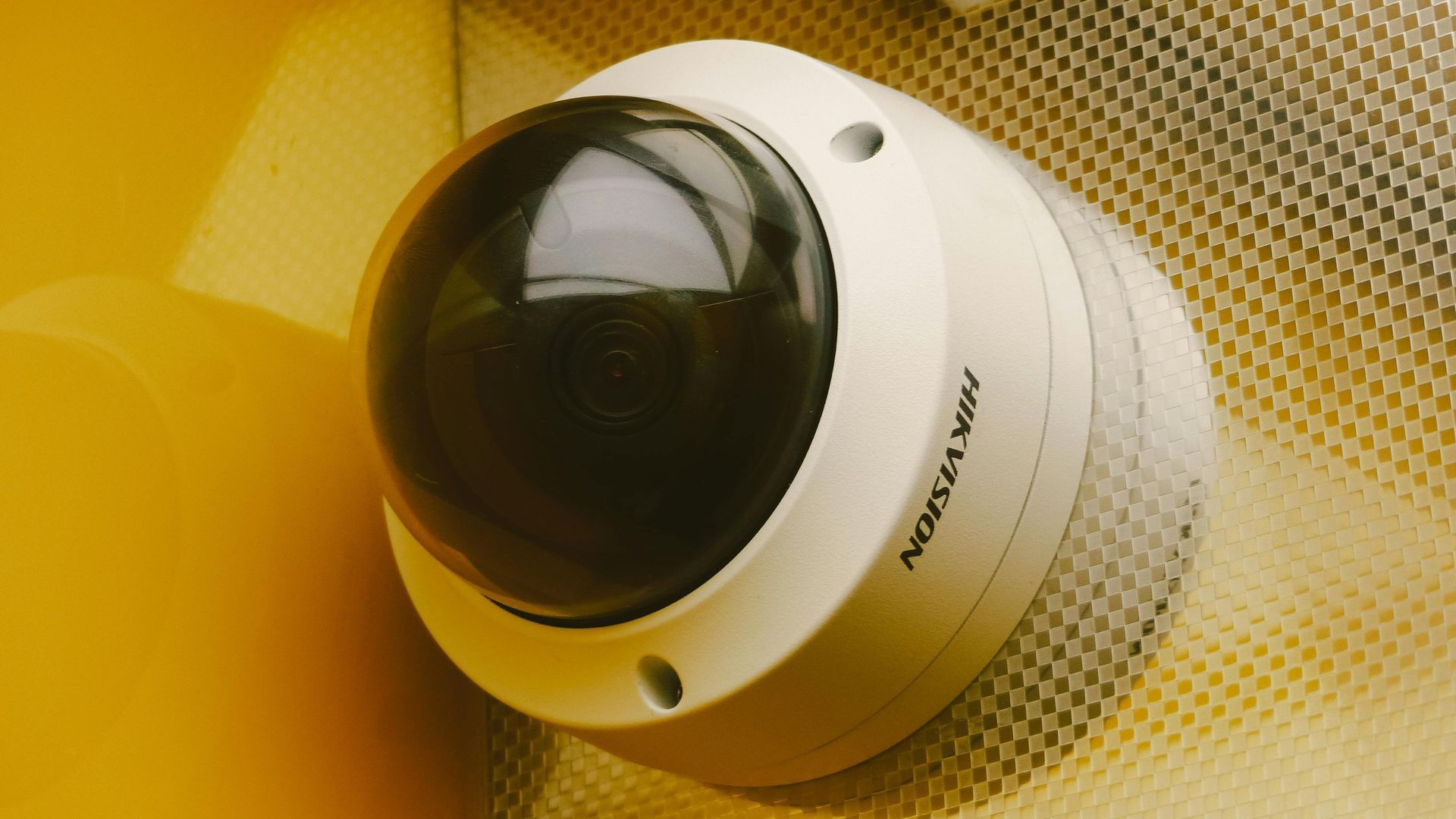 White dome security camera on a yellow perforated wall.