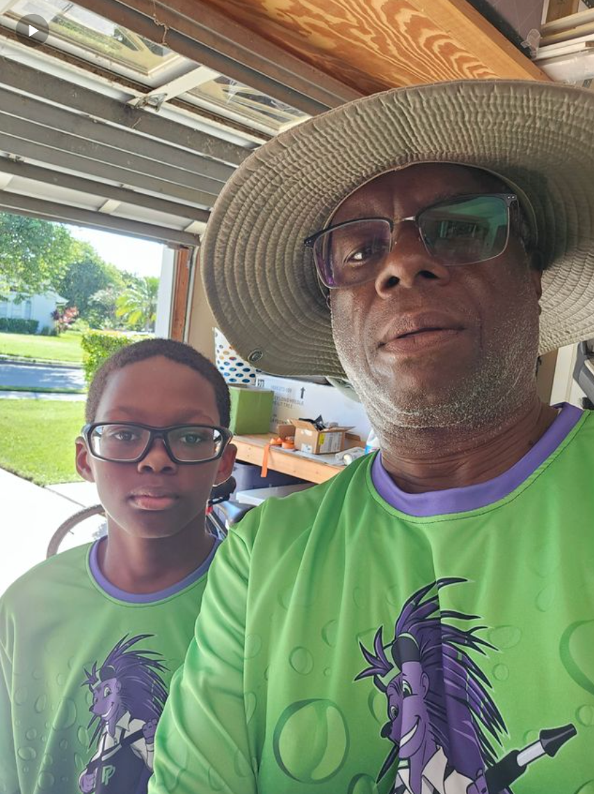 Two people in matching green shirts and sunglasses taking a selfie in a covered outdoor area.