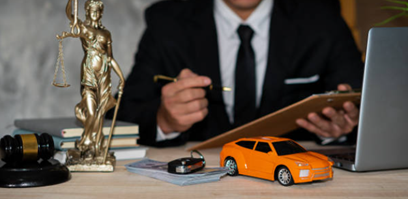 A man in a suit at a desk with a laptop and a car model, symbolizing an auto accident attorney.