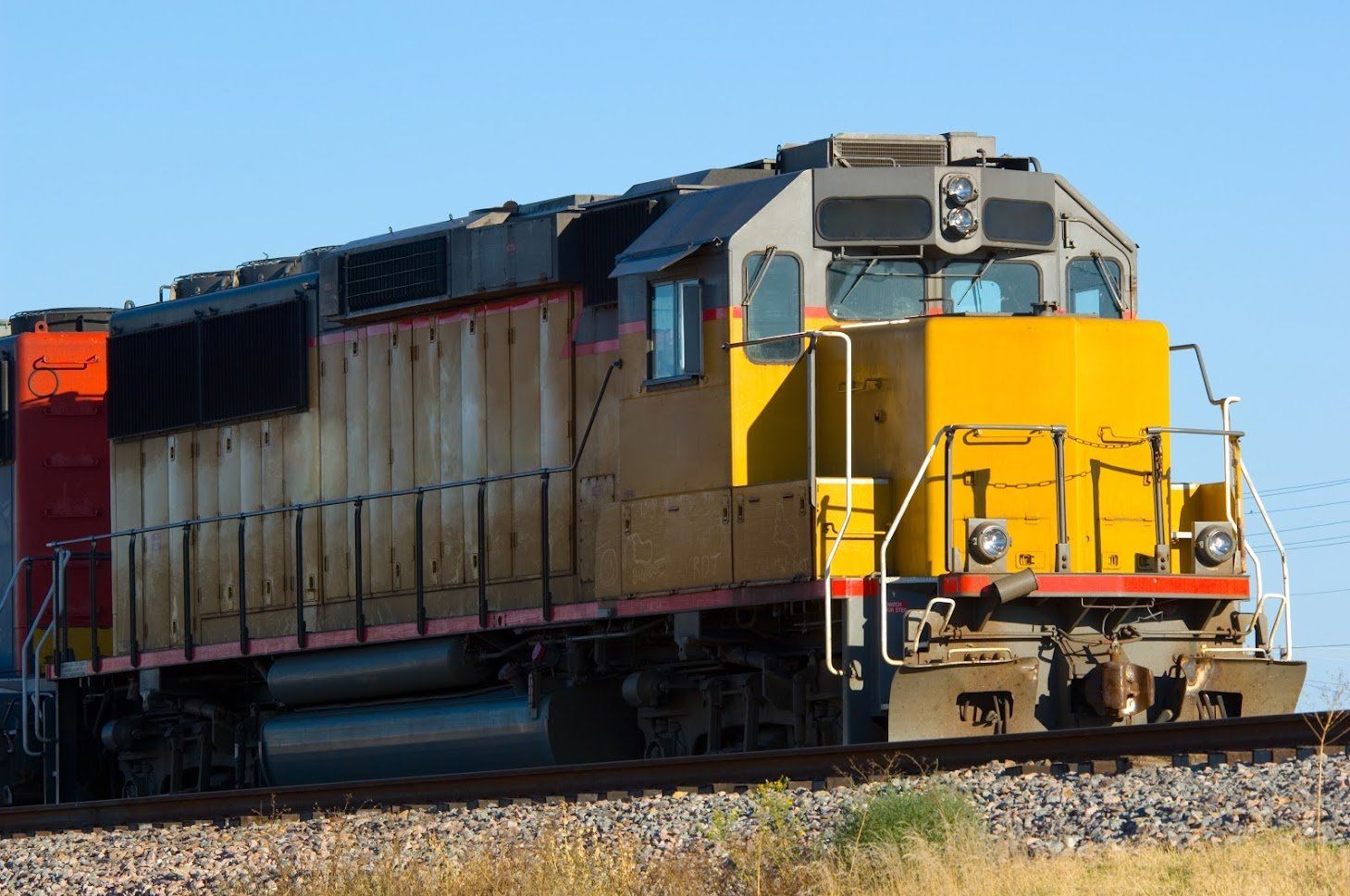 Yellow and rusty freight train engine on tracks under a blue sky.