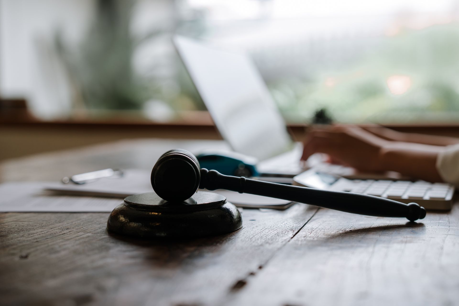 A gavel and legal documents on a desk, with a lawyer working on a laptop in the background.