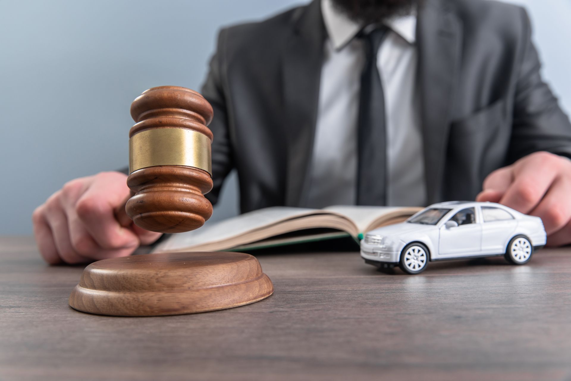 A judge’s gavel sits on a desk beside a small car model and an open legal book.