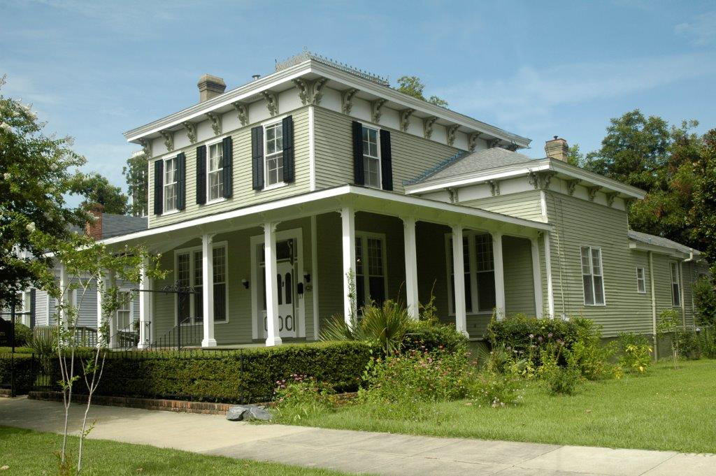 Light green two-story house with white porch columns, black shutters, and decorative trim.