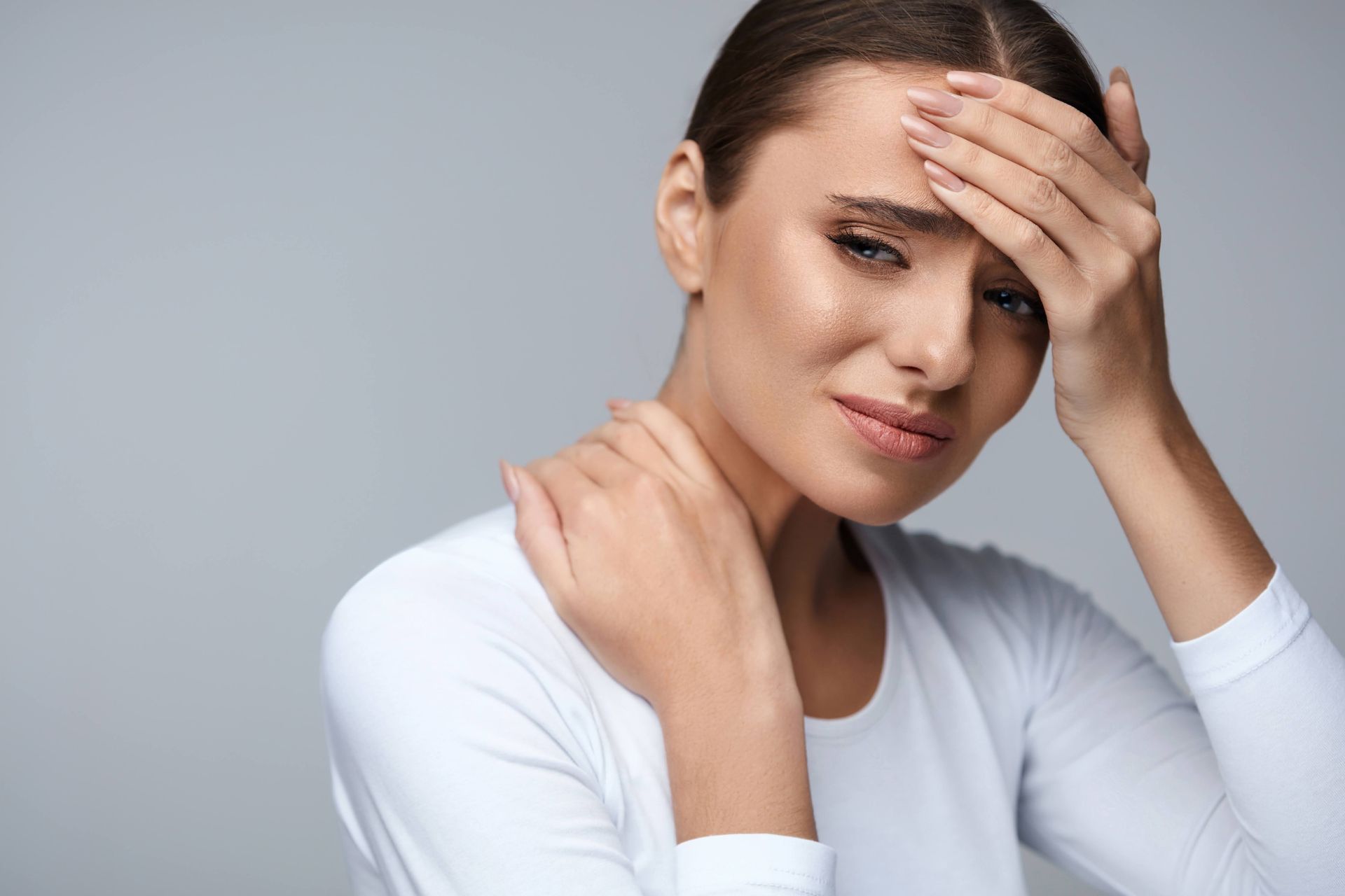 Woman with hand on forehead and neck, showing signs of a headache.
