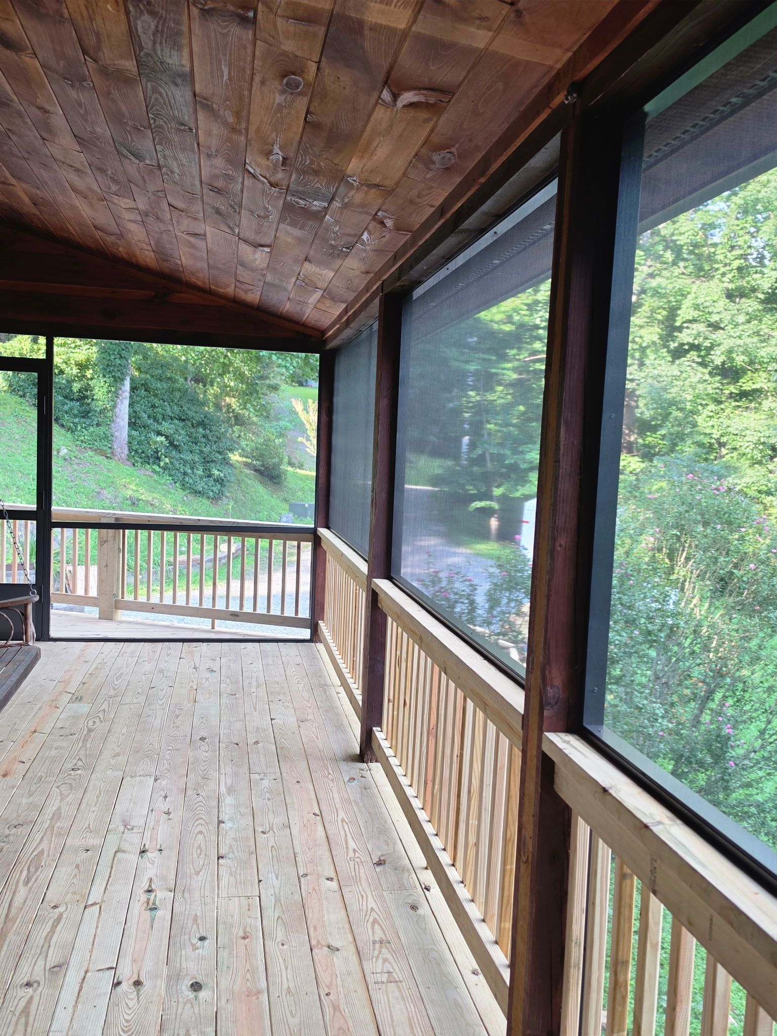 Wooden covered porch with screened windows overlooking a green wooded area