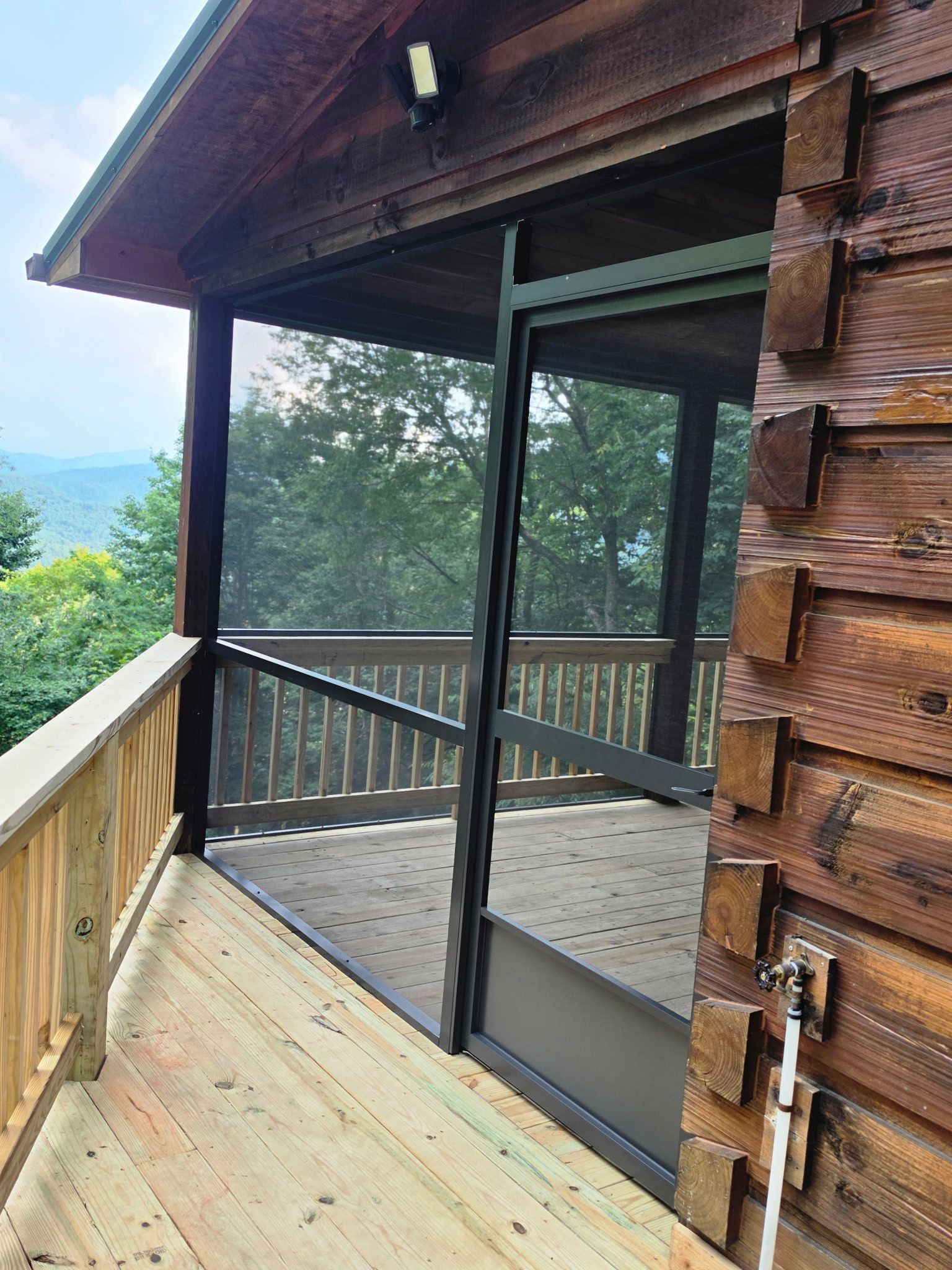Wooden cabin porch with screened railing and view of green mountains beyond