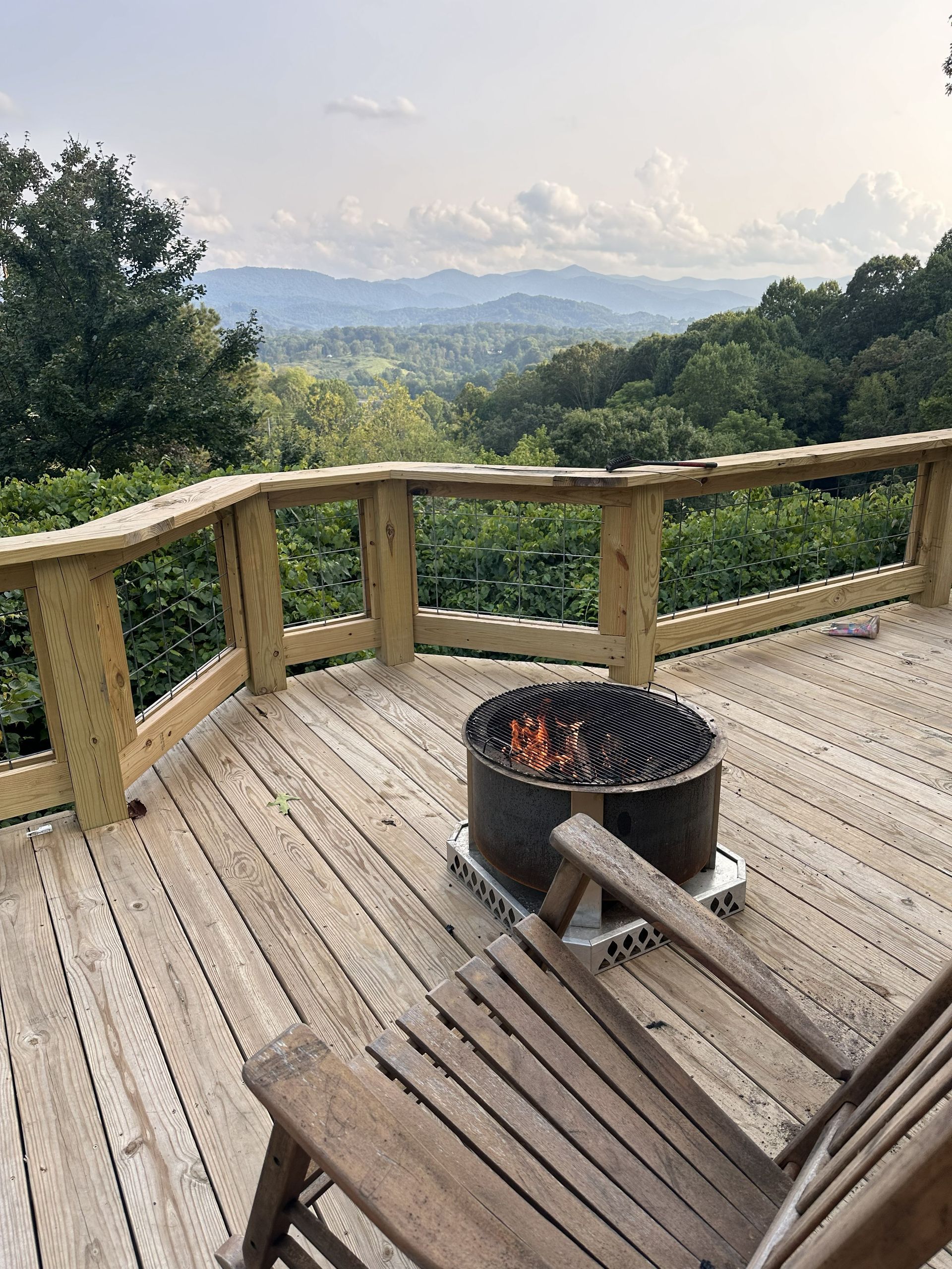 Wooden deck with fire pit and chair overlooking a misty mountain landscape