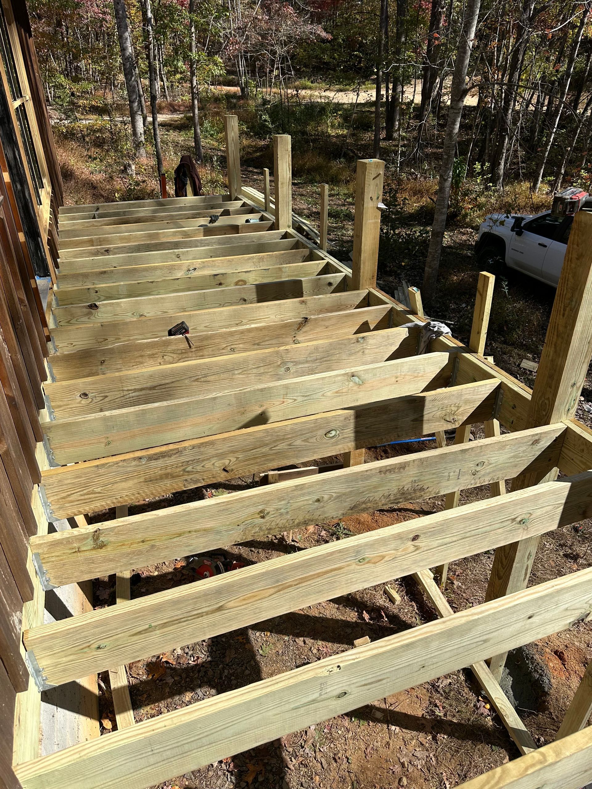 Unfinished wooden stair frame on a wooded hillside, with posts and beams in sunlight.