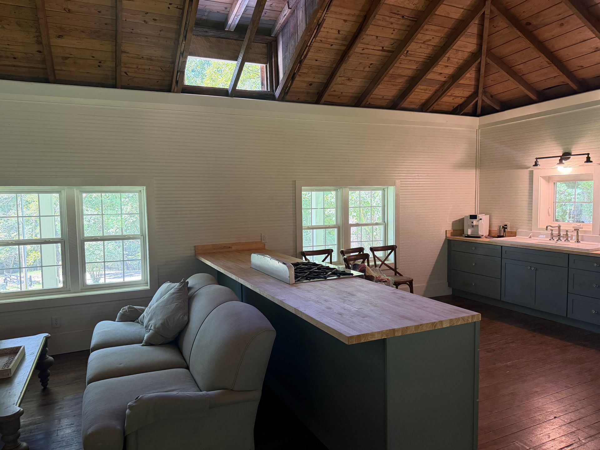 Living room with gray sofa, wood ceiling, open kitchen island, and large windows
