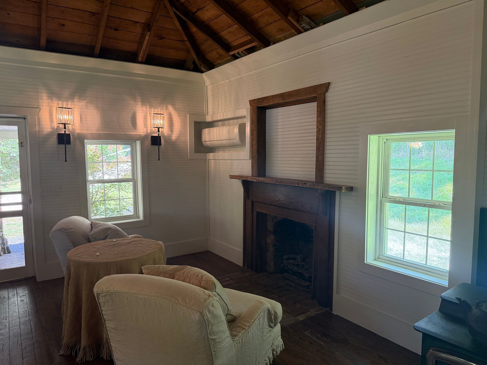 Cozy living room with white walls, wood ceiling, fireplace, windows, and wicker chairs