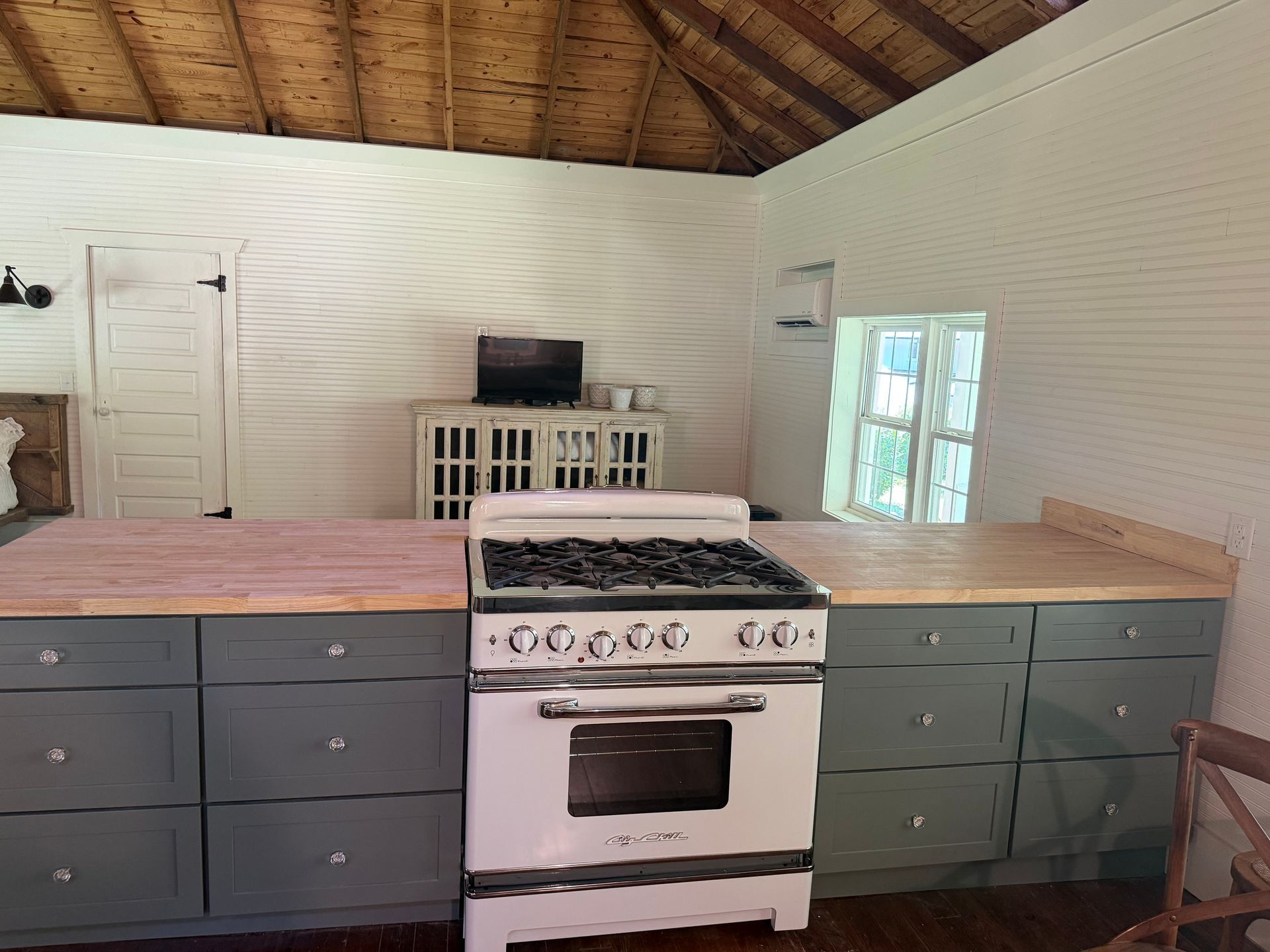 Kitchen with white stove, gray cabinets, wood countertops, and a vaulted ceiling.